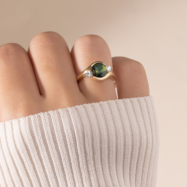 Green Oval Cut Gemstone Paired With A Pear Shaped Diamond Positioned In a Ribbon Band