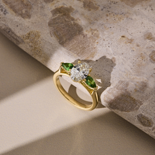 oval cut diamond with emerald side stones on a yellow gold band